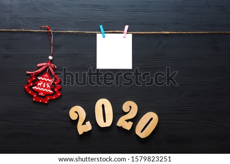 New Year greeting card. Brown cardboard sheet of paper hanging on a rope with a clothespin on a dark wooden background. Christmas toy. 2020.