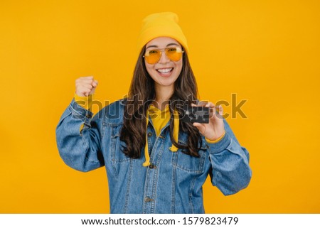 Young asian girl showing credit card isolated over yellow background