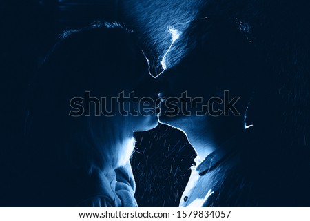 Silhouette of young happy couple in love kissing in the night under rain, toned in blue