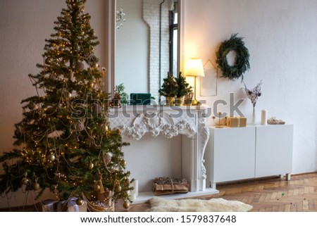 Christmas decoration in living room at home. In white classic interior with lighting. New year inspiration. Wreath and traditional decor. Fireplace and gifts under the tree.