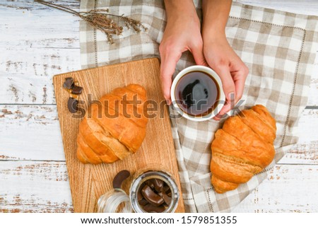 Girl holds a coffee mug. on the background of a croissant. coffee with a croissant. the beginning of the morning. Coffee cup. Top view on woman's hands holding a cup with coffee and fresh french