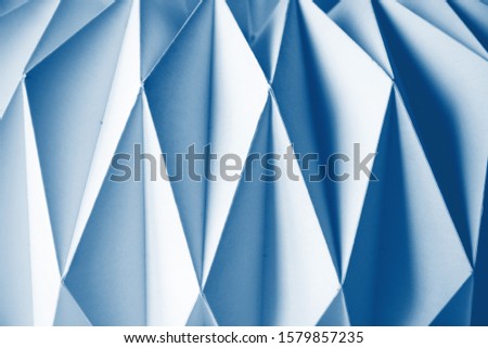 Macro classic blue image of white paper folded in geometric shapes, three-dimensional effect, abstract background. Out of focus. Trendy color 2020 classic blue.
