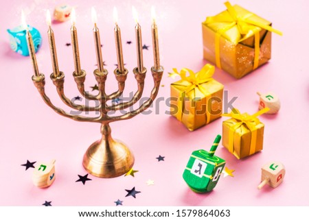 Happy Chanukah background with menorah, burning candles, gift boxes, dreidel spinnners and donuts on pink. Space for text