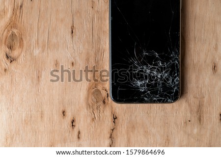 Closeup of black smartphone with broken screen on wooden background. A close up picture of mobile phone with broken screen.