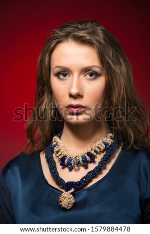 Beautiful young brunette woman in stylish casual clothing with accessories standing over red wall in photo studio. Fashion and beauty concept
