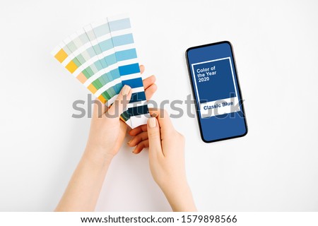 Female hand holding color swatches and  smartphone with color of the year 2020 - Classic Blue. Color trend palette. 