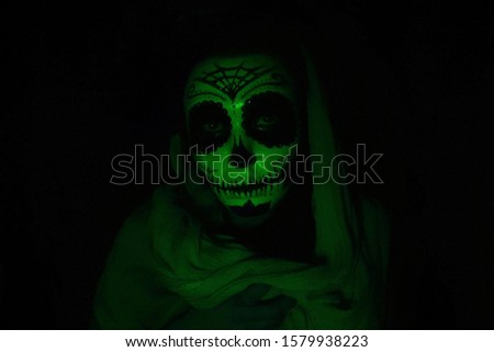 Halloween mask Catrina. Mexican day of the dead. Portrait of a young woman with scary makeup for Halloween on a dark background.