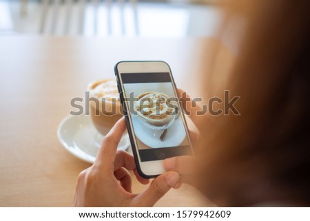 The hand of the woman using a smartphone to take photo of a coffee