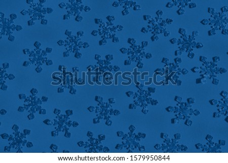 Textured foil snowflakes confetti sparse on trendy blue colored background. Simple holiday concept. Winter festive backdrop. Top view, flat lay. Color trend concept.