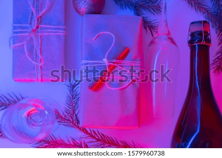 Christmas presents in sustainable package in neon lights. New Year party concept: gifts, beverage and glasses in pink and blue background, top view