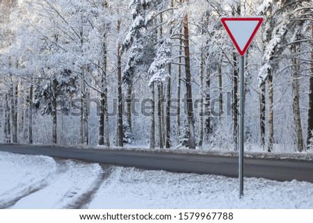 crossroads with main road and yield sign on it in winter forest road