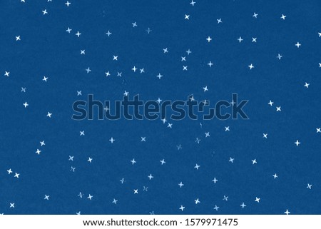 Metallic foil stars confetti sparse on trendy blue colored background. Simple holiday concept. Winter festive backdrop. Top view, flat lay. Color trend concept.