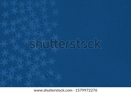 Metallic foil snowflakes confetti sparse on trendy blue colored background. Simple holiday concept. Winter festive backdrop. Top view, flat lay. Color trend concept. Copy space for text.