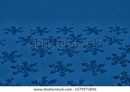 Textured foil snowflakes confetti sparse on trendy blue colored background with copy space. Simple holiday concept. Winter festive backdrop. Isometric flat lay, open composition. Color trend concept.
