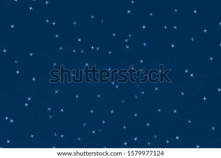 Metallic foil stars confetti sparse on trendy blue colored background. Simple holiday concept. Winter festive backdrop. Top view, flat lay. Color trend concept.