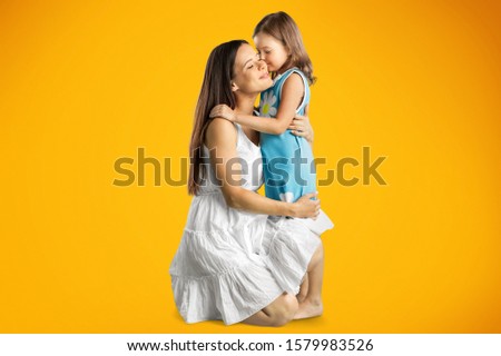 Mommy little kid daughter isolated on yellow background studio portrait