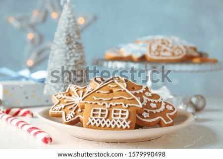 Plate with Christmas cookies, Christmas trees, toys, gift boxes on white table, against blue background, closeup