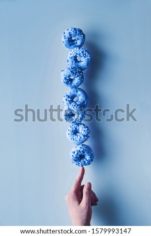 Creative monochrome image toned in blue color. Concept of perfect balance. Tower or pyramid of donuts balancing on index finger. Chanukah dessert. Classic blue, color of the year 2020. 