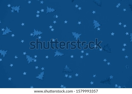 Metallic foil christmas trees and stars confetti sparse on trendy blue background. Simple holiday concept. Winter festive backdrop. Top view, flat lay. Color trend concept.