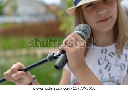 Young girl holding mic with two hands. Microphone and unrecognizable girl singer close up. Cropped image of female teen singer in the park. Copyspace
