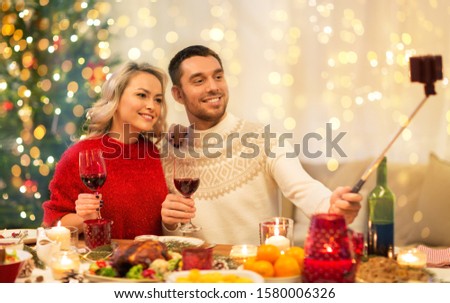 christmas, holidays, technology and people concept - happy couple in taking picture by selfie stick at home dinner