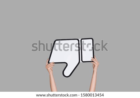 Hands holding the sign of dislike on grey studio background. Negative space to insert your text or image, advertising. Social media, showing meaning, communication, gadgets, modern technologies.