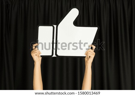 Hands holding the sign of like on black studio background. Negative space to insert your text or image, advertising. Social media, showing meaning, communication, gadgets, modern technologies.
