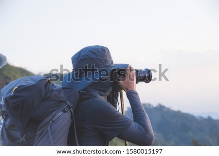 young man backpacker hiking on mountain peak and take photo and holding camera, subject is blurred. selected focus