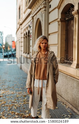 Beautiful blonde woman walking through the autumn streets of the city using a modern smartphone, a hipster blogger woman using her cellphone