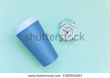 Simply flat lay design paper coffee cup colored in trendy color of year 2020 Classic Blue. and alarm clock isolated on blue pastel background. Top view copy space.