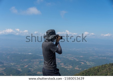 young man backpacker hiking on mountain peak and take photo and holding camera, subject is blurred. selected focus