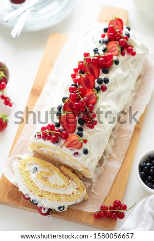 Cutted sponge biscuit cake roll filling whipped cream and berries decorated strawberry, blueberry and red currants on white wooden background. Soft focus. Summer food concept