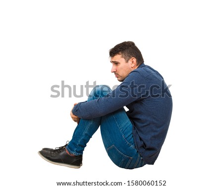 Full length side view of upset and depressed man introvert sitting alone on the floor looking scared isolated over white background. Helpless guy victim of bullying or abuse. Royalty-Free Stock Photo #1580060152