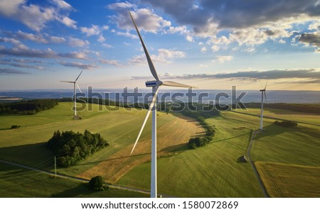 Aerial view of wind turbine farm. Wind power plants in green landscape against sunset sky with clouds. Aerial, drone inspection of wind turbine. Royalty-Free Stock Photo #1580072869