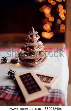 Christmas tree made of natural chocolate stands on the festive table against the background of lights, cozy home atmosphere