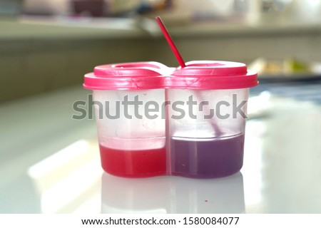 a double jar of water to scrub the brush is on the table. water is colored in purple and red. childish creation