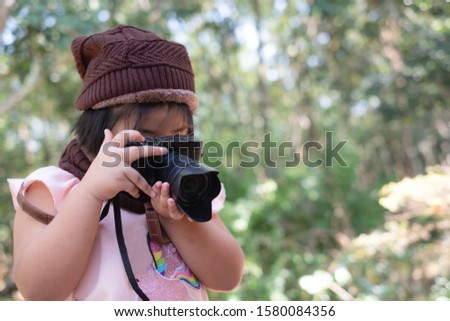 Portrait of cute little girl in Wool hat taking a picture with digital camera on blurred background. Photography concept