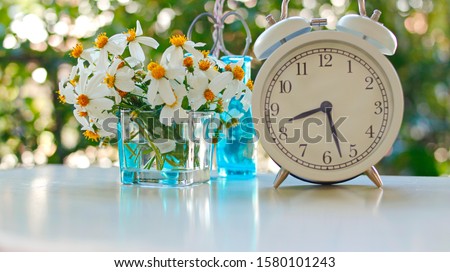 White alarm clock With the backdrop of a vase of fresh flowers placed on a wooden table
