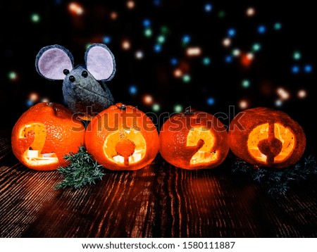 New Year picture. The gray toy rat is a symbol of the coming year against the background of multi-colored garland lights with 2020 tangerine lights, coniferous branches, nuts and spices on a wooden su