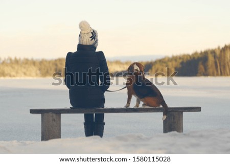 A young woman with a dog sitting on a wooden bench on the shore of a frozen lake.