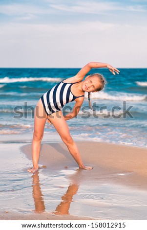 Beautiful little girl excercising on the beach outdoor