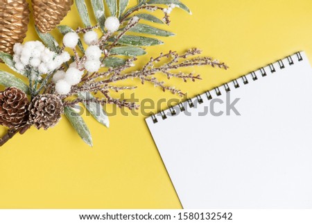 Beautiful christmas decoration. Christmas tree branch pine cones and paper notepad , on a yellow background. Plnans fof new year.