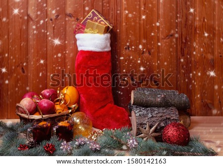 Wicker basket with fruits, fluffy christmas stocking, mulled wine, pile of firewood and christmas balls. View with copy space.