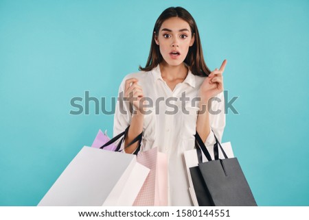 Attractive casual girl with shopping bags amazedly looking in camera having idea over colorful background