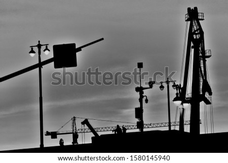 Abstract black and white photo of construction cranes and small city silhouettes