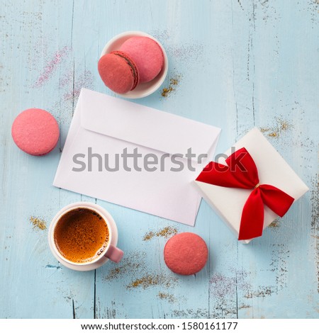 Valentines day, birthday, wedding or other holiday composition. White envelope, cup of coffee, macaroons and small gift on wooden blue background. Copy space for text. Flat lay
