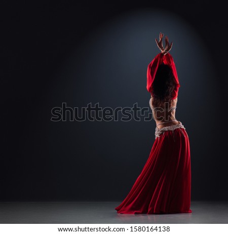 beautiful black-haired girl in a red ethnic dress on the stage dances oriental dancing with her back Royalty-Free Stock Photo #1580164138