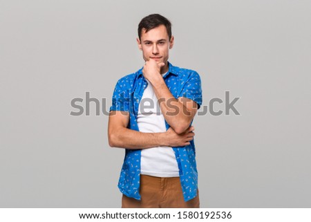 Thoughtful young handsome man is thinking attentively and looking at the camera isolated over grey background.