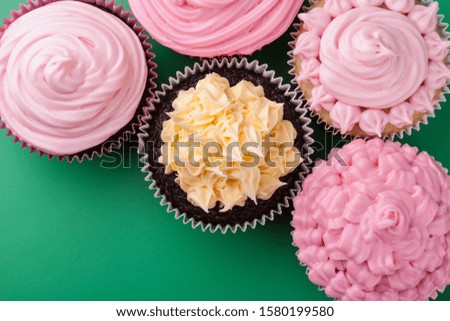Delicious varietey of vanilla and chocolate sweet cupcake with pink icing sugar, green background