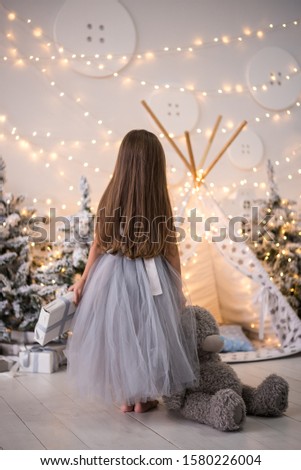 Happy funny child girl with gifts at the Christmas tree.  Little girl picture in the New Year decorations.  New Year's advertising.  Photo studio with christmas decoration.